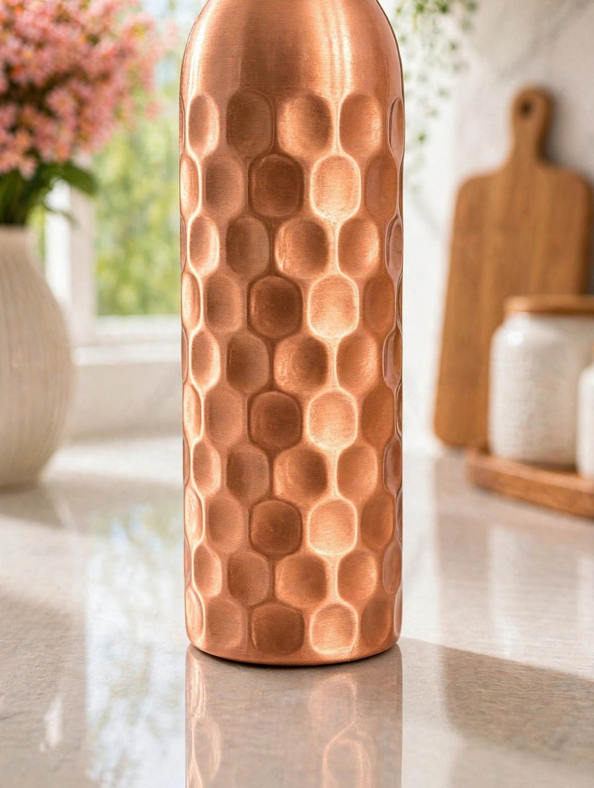 Close-up of the lower body and base of the hammered copper bottle on a marble countertop